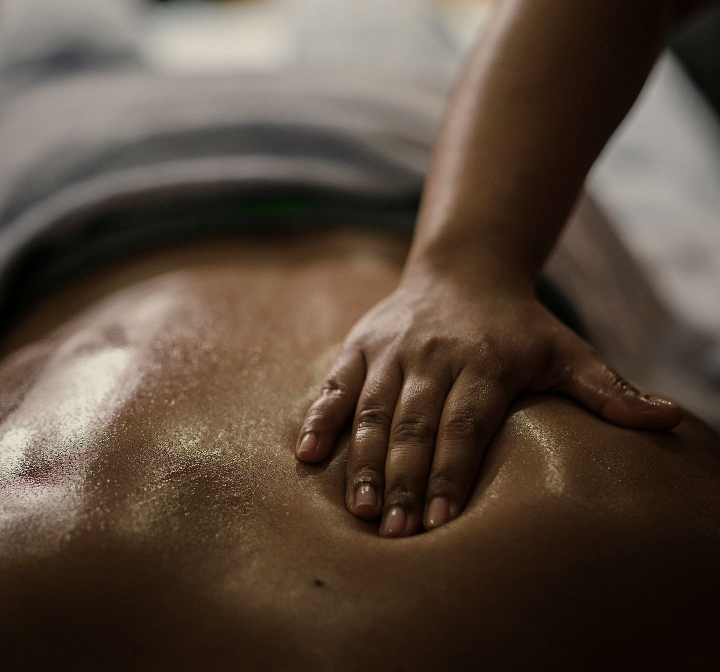 Ritual Noche: una mano trabajando con aceite tibio sobre la espalda, en penumbra.